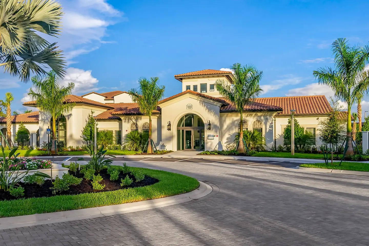 Alternate view of clubhouse and leasing office with tropical landscaping and roundabout driveway and parking